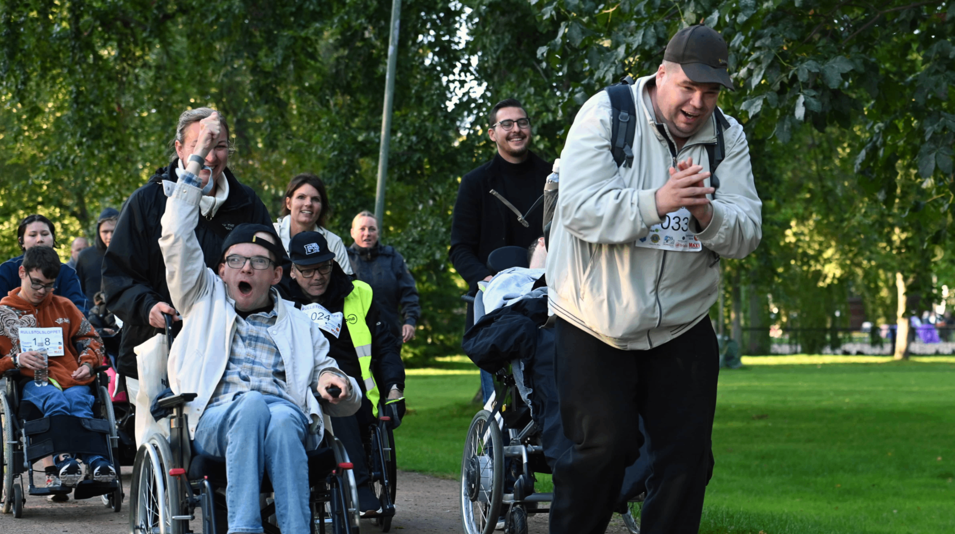 En kille i rullstol som tjoar och sträcker upp handen i luften. En gående man som klappar händerna av lycka.