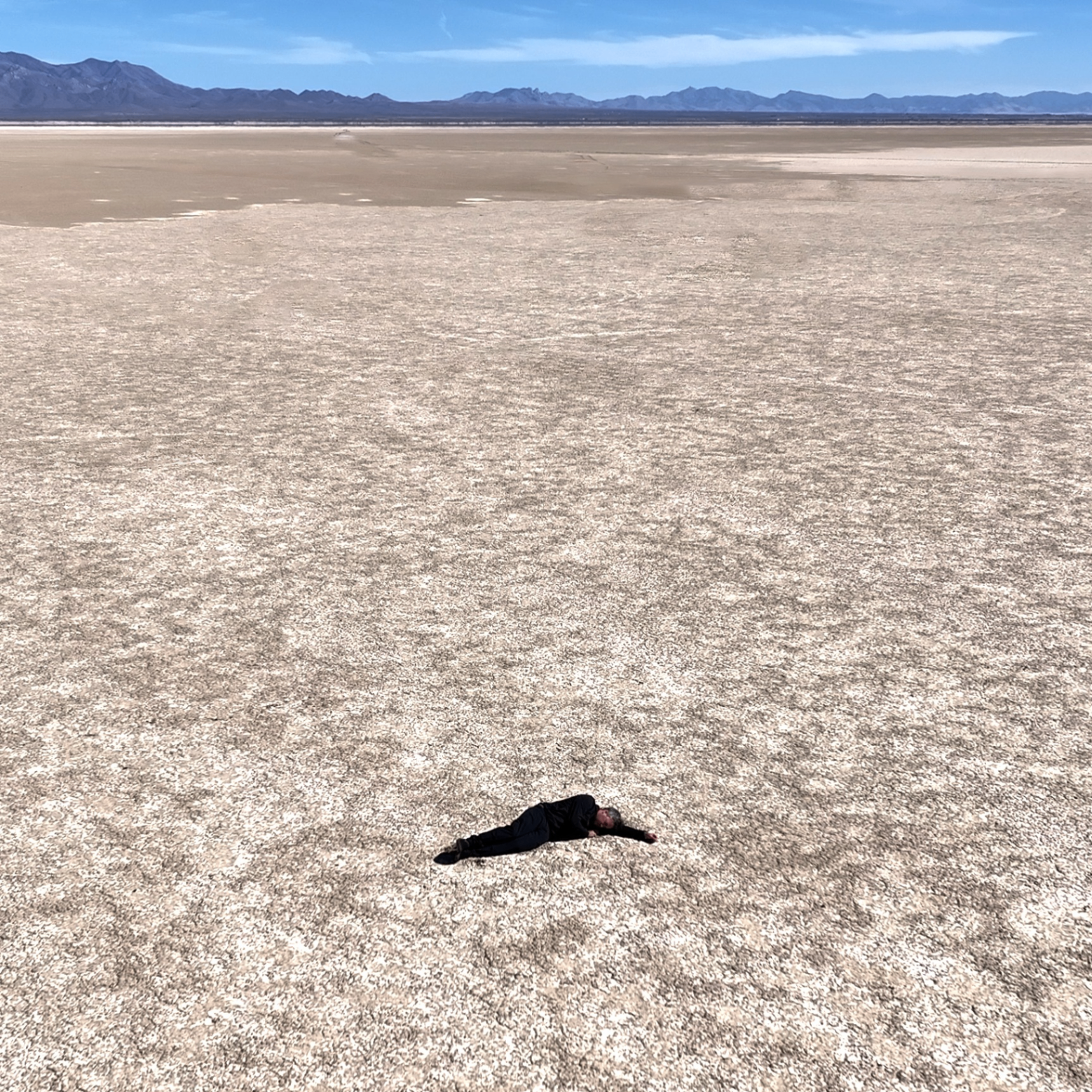 Artist Rick Silva lies in an expansive salt flat that occupies most of the video still. A sliver of sky and a distant mountain range can be seen on the horizon
