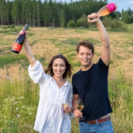 Man and woman in field holding corollary brand wine above their heads