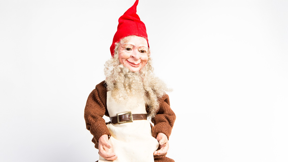 docka i form av en gammeldags tomtenisse med bruna kläder, skägg och röd luva