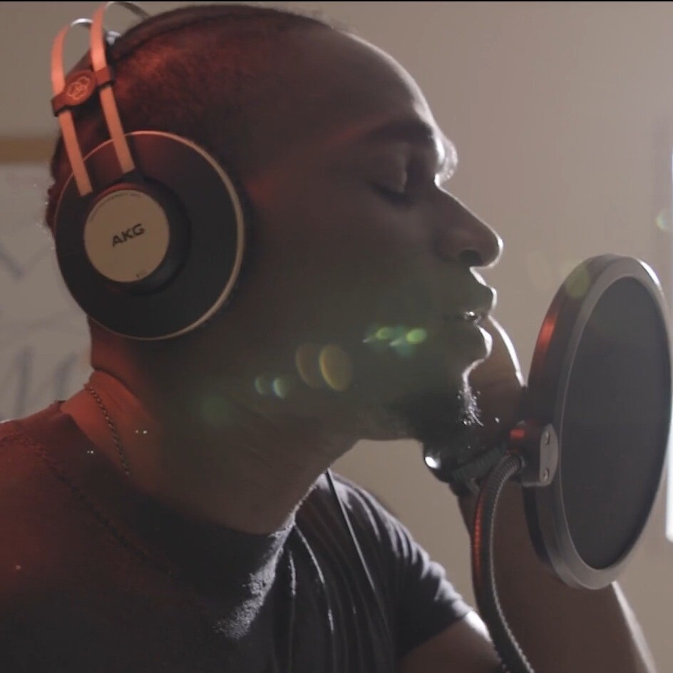 Incarcerated man in sound studio singing with eyes closed into mic. Emotional expression.