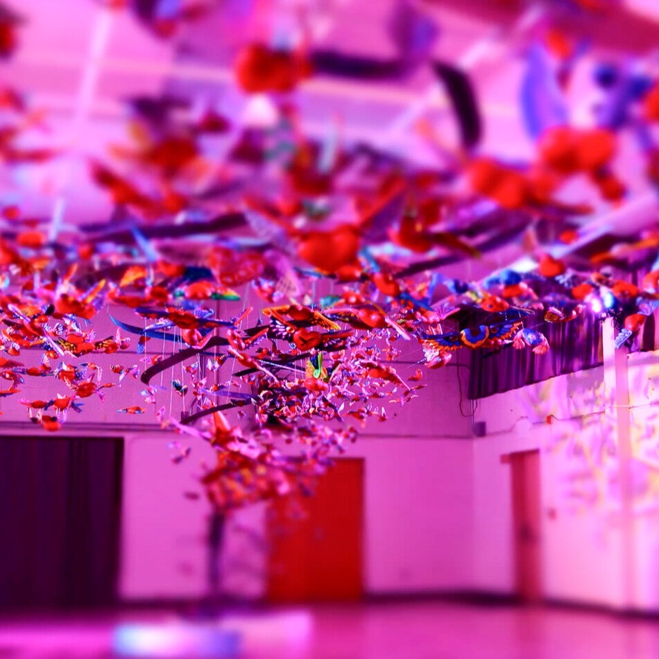 Hundreds of winged hearts suspended in gymnasium. Pink hued throughout.