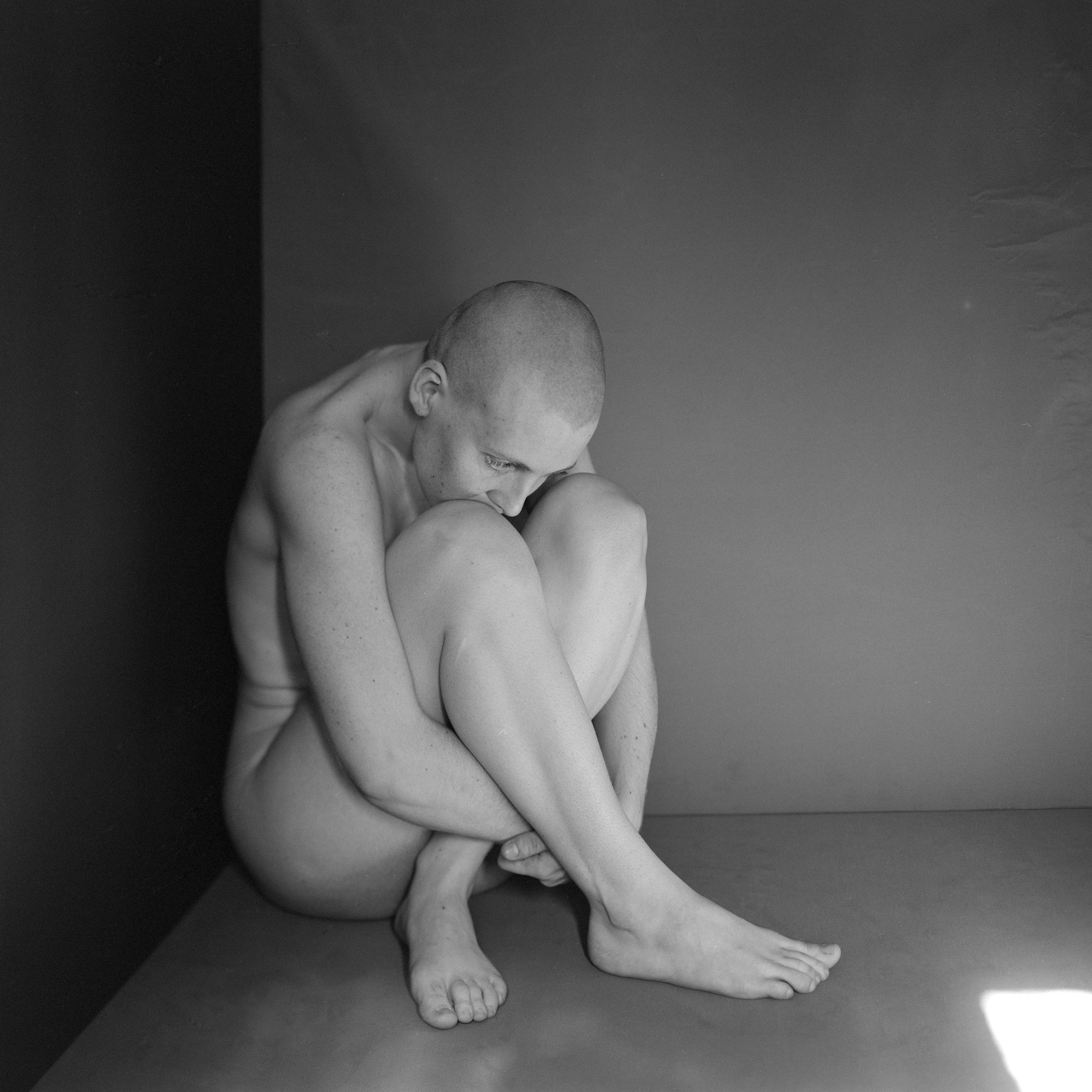 a naked person curled into a ball in the corner of a room