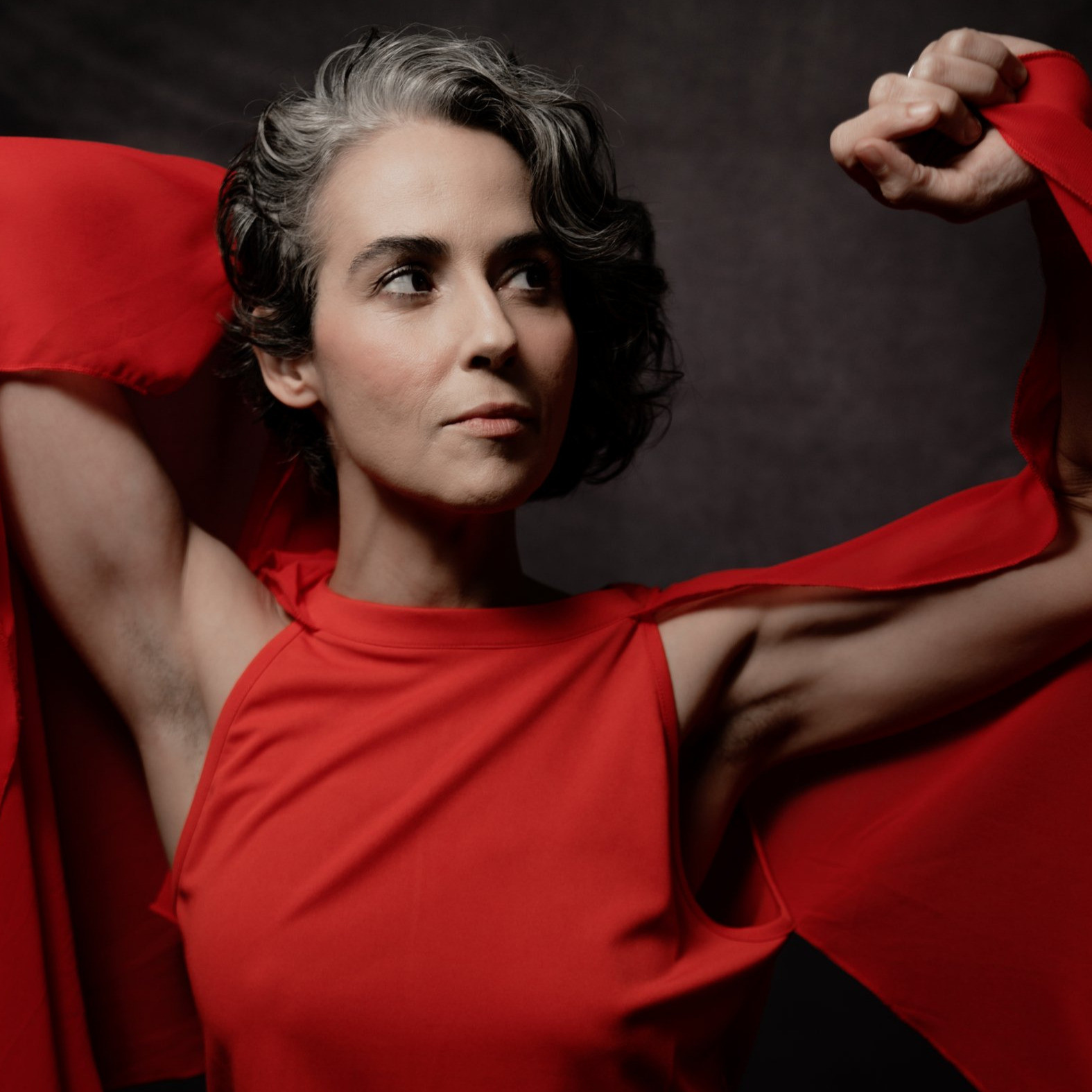 Clarice Assad wearing a red dress with her arms up and looking to the side.
