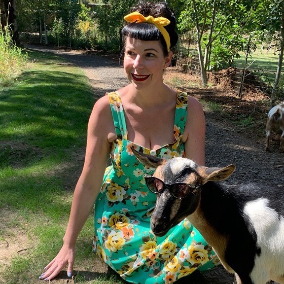 a woman in a flower dress and a goat in sunglasses