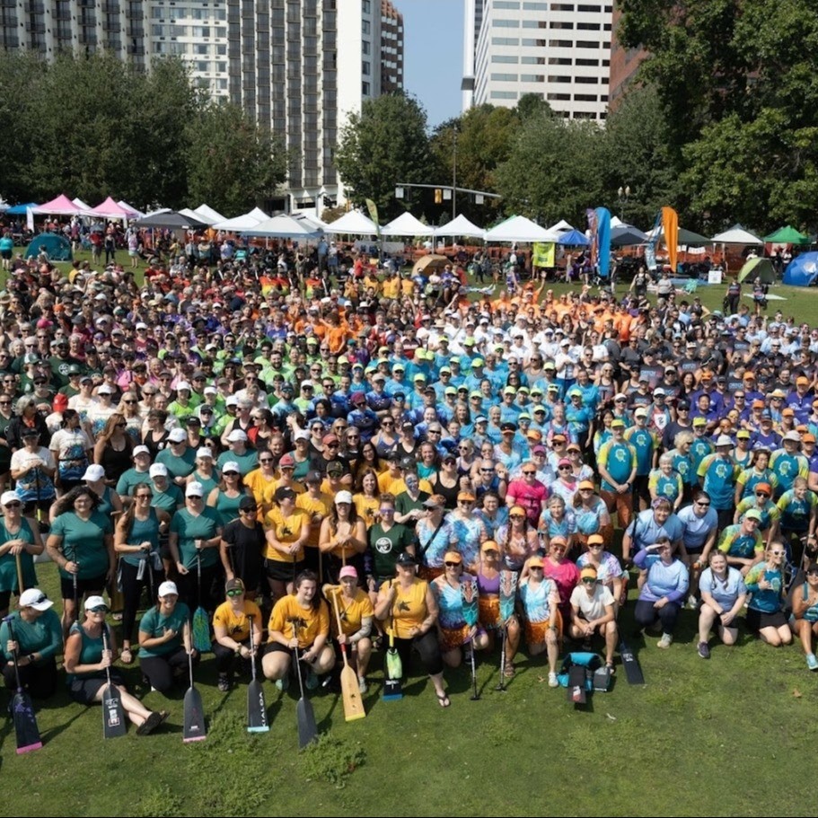 a large crowd of dragon boat teams pose on a lawn