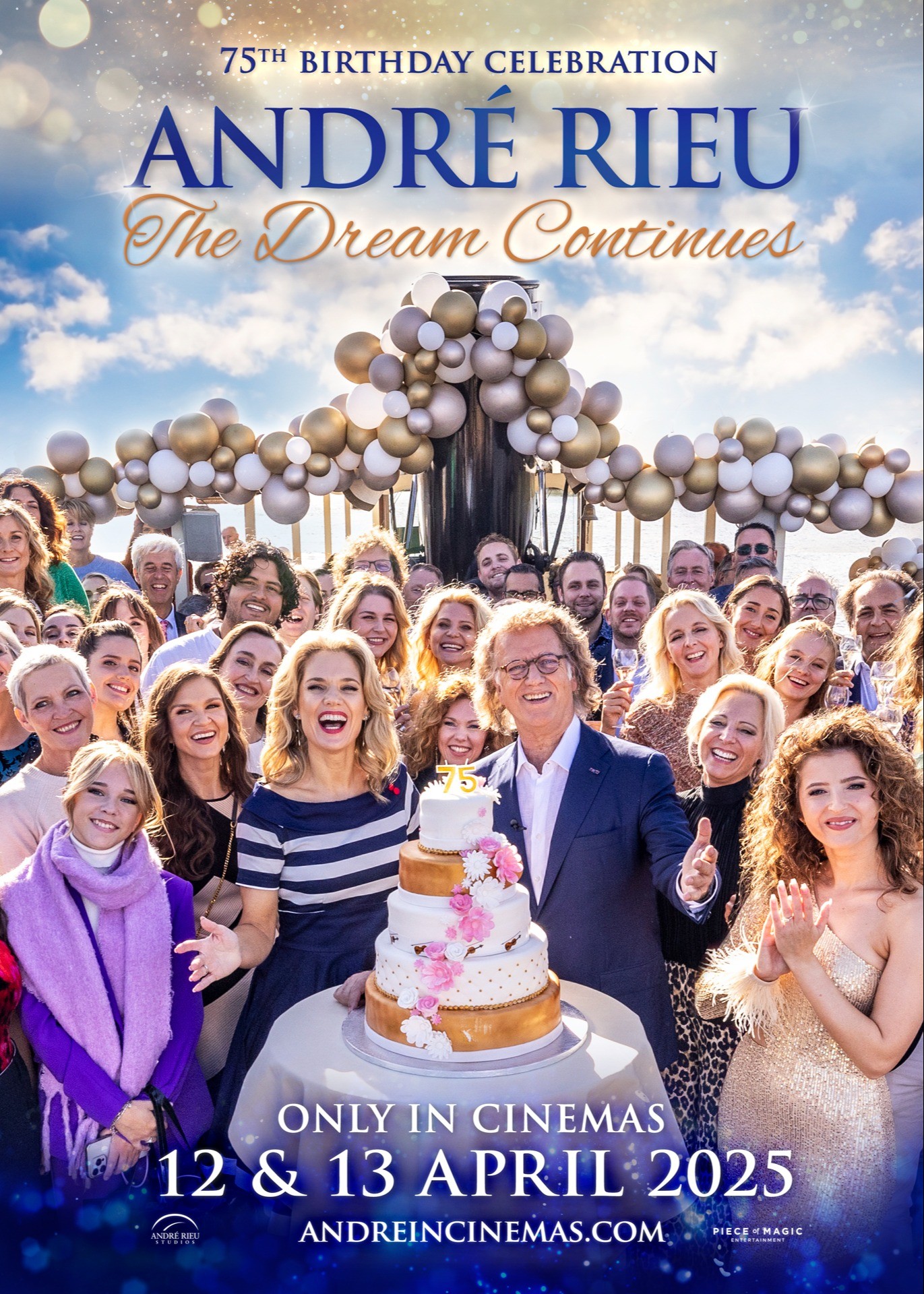 Andre Rieu står och håller en tårta med ljus i form av 75 på. Runt honom står flera glada, firande personer.