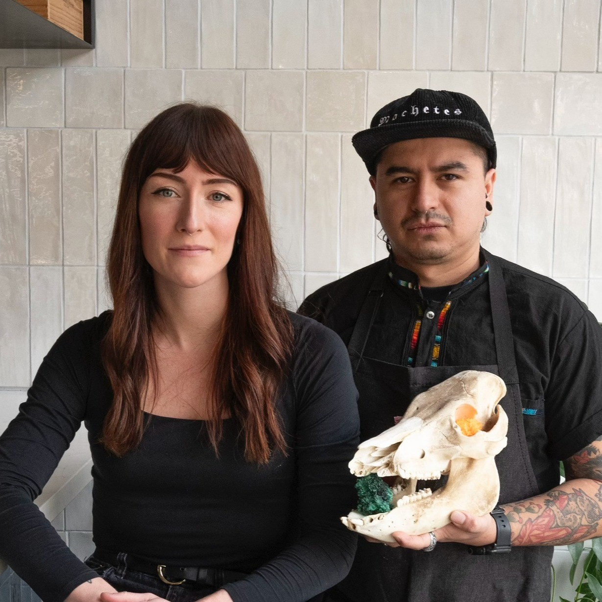 two people looking at the camera, on is holding a cow skull