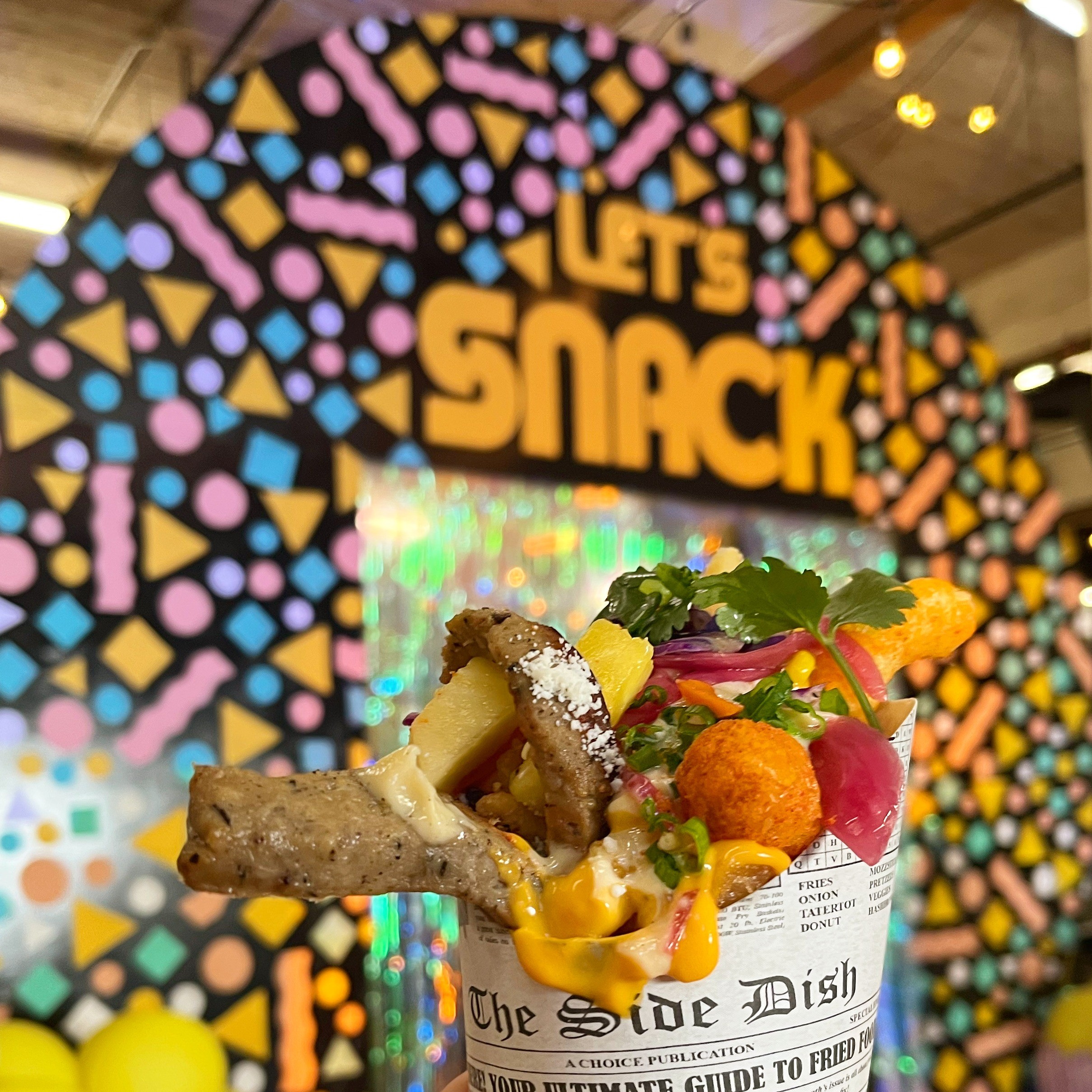 image of hand-held food in front of sign saying "let's snack"