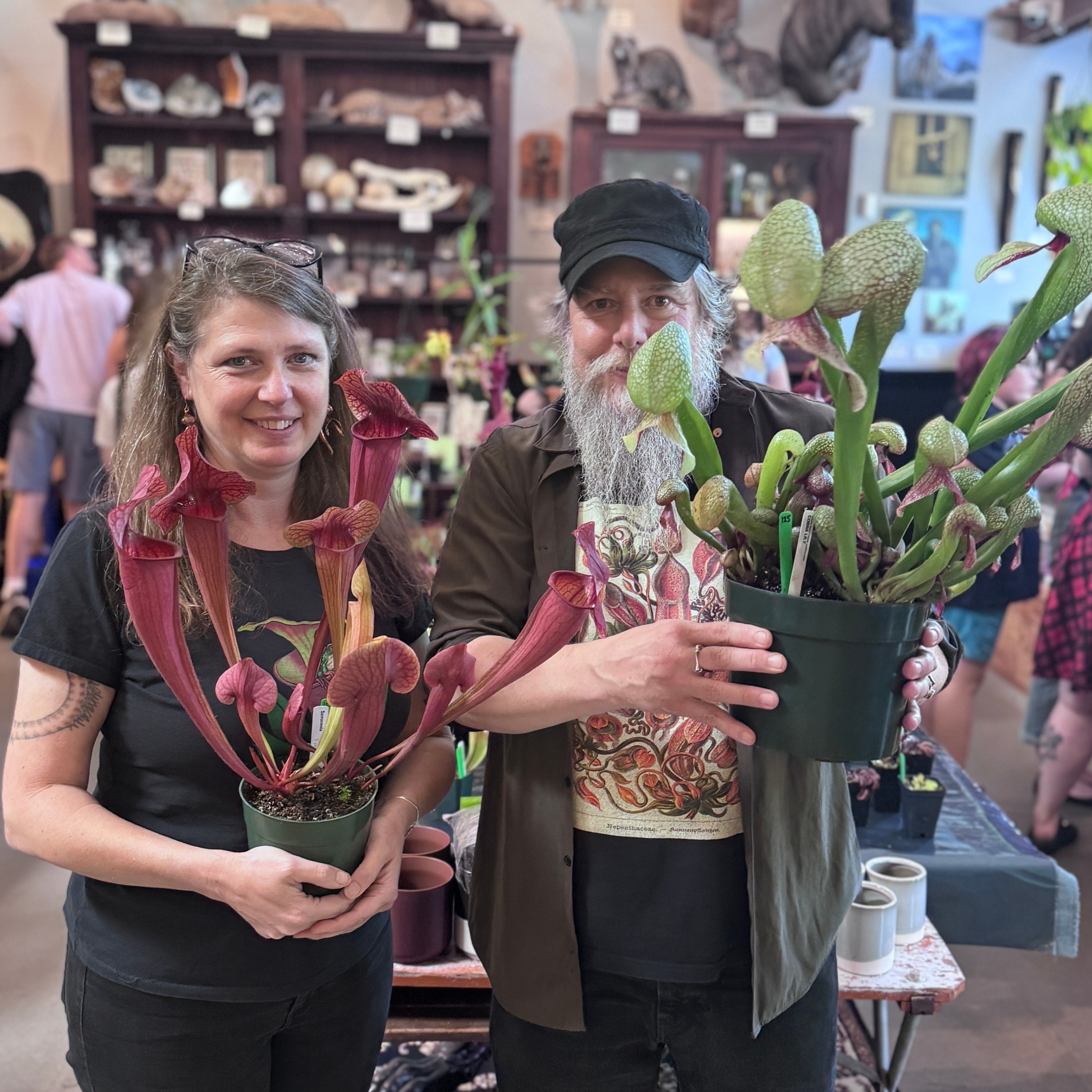 two people hold up carnivorous plants in pots