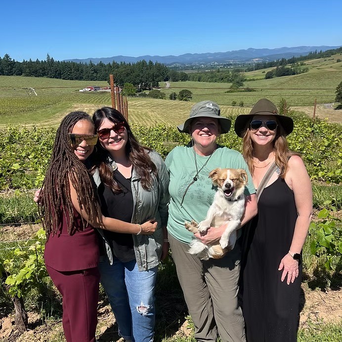 people and a dog standing in front of fields of grapes