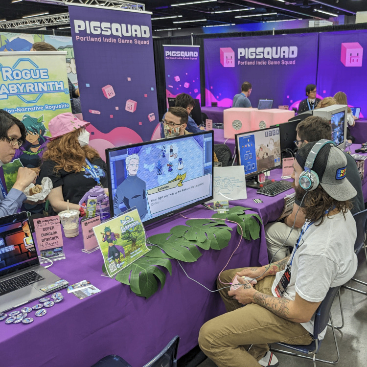 A photo of a PIGSquad showcase event. There are several people showcasing and playing indie games.