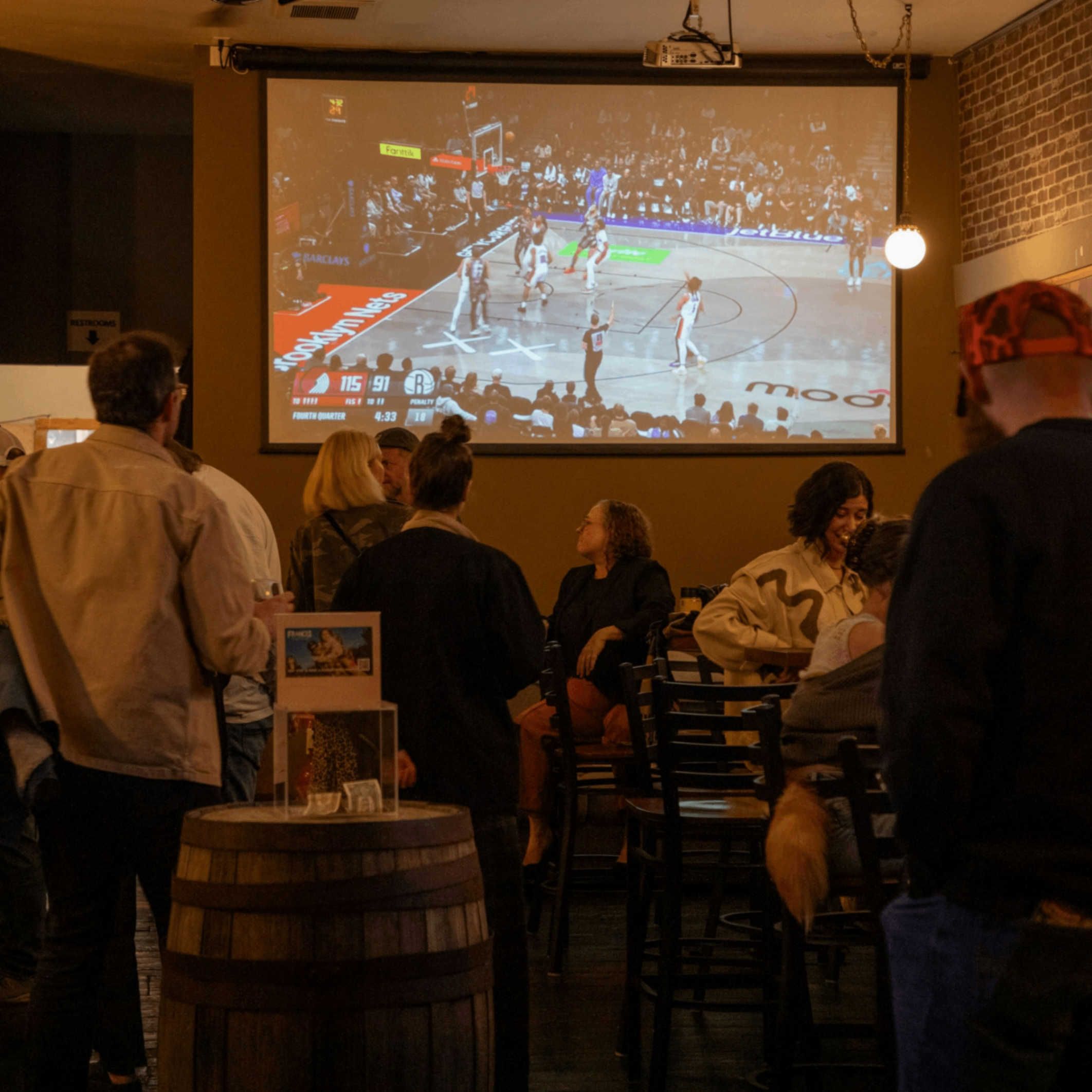 people mingling inside a bar under a large screen television