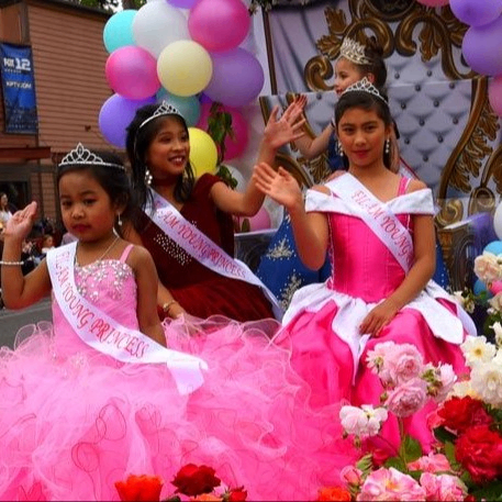 girls in frilly pink dresses waving from a parade float