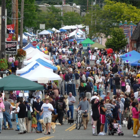 a busy street fair with crowds of people and vendor booths lining the street