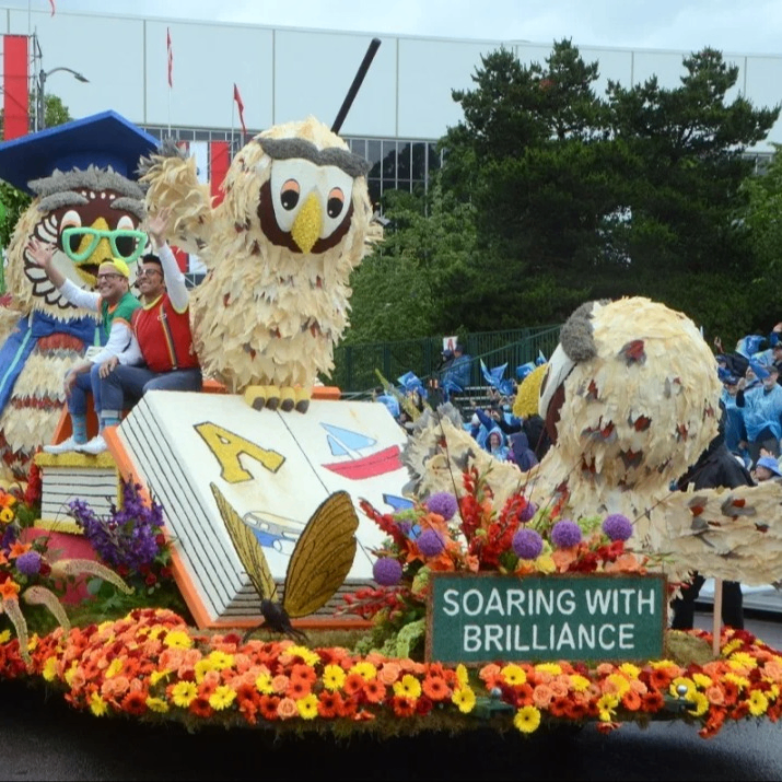 an elaborate parade float featuring owls reading a large book