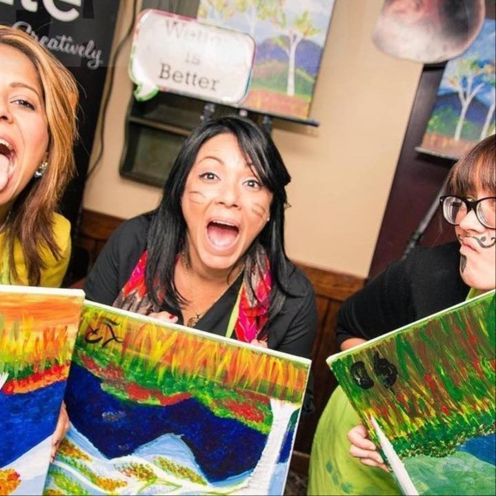 people smiling and holding up newly painted canvases 