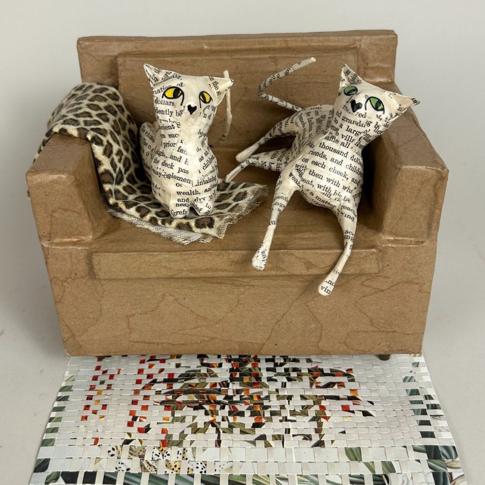 2 paper mache cats lounging on a paper sofa